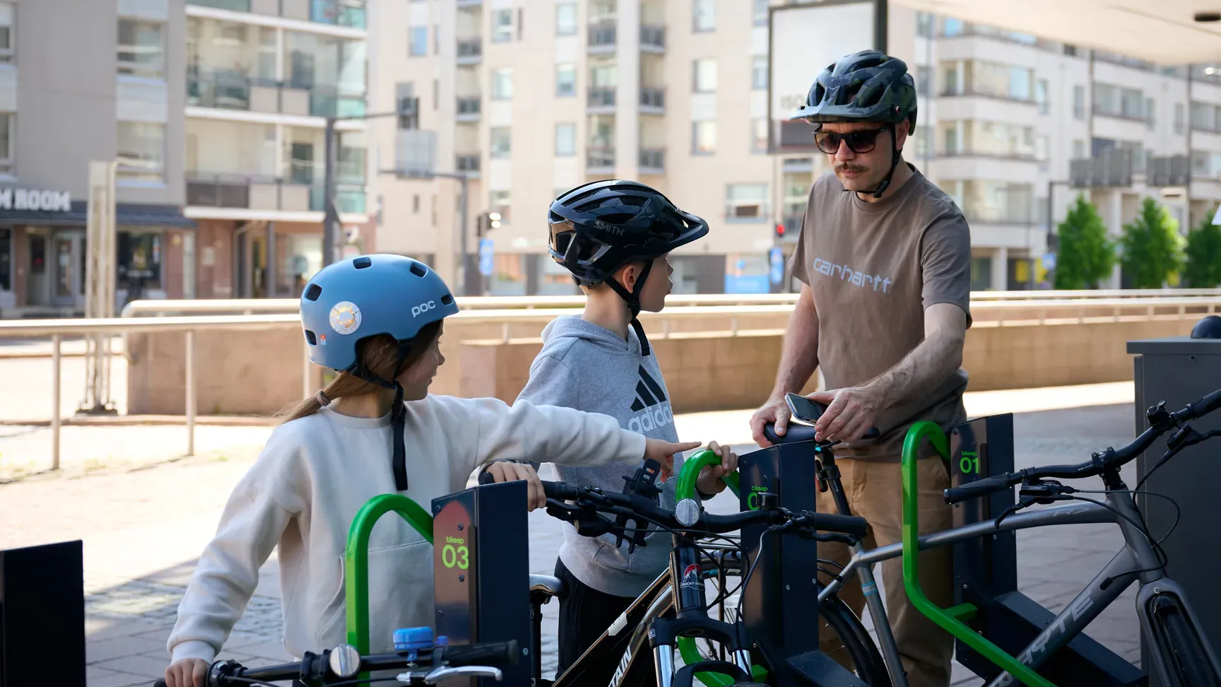 An adult and two children on bicycles docking at a Bikeep smart bike parking station in Finland