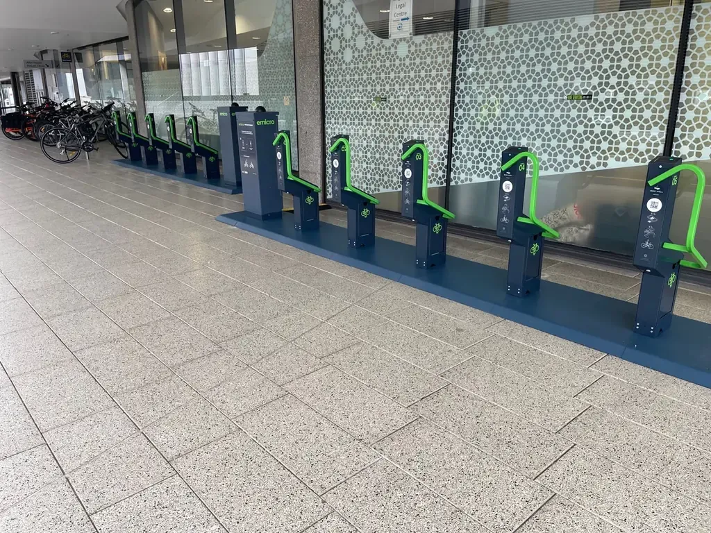Two rows of Bikeep e-bike charging docks with green locking bars under a covered walkway outside the Law & Justice Library at UNSW Sydney