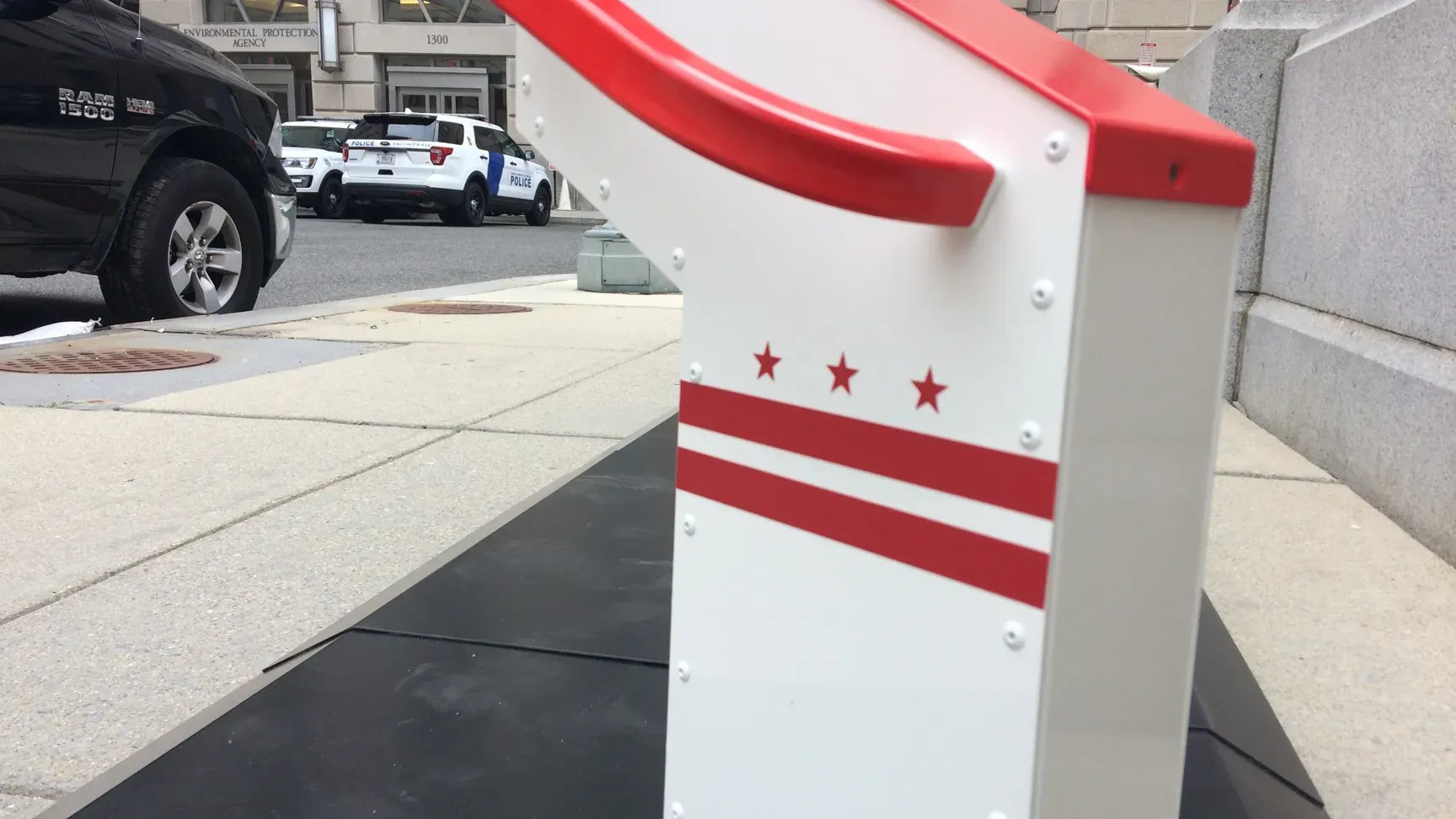 A white and red Bikeep dock with the stars and bars of the DC flag outside the Wilson Building in Washington, DC